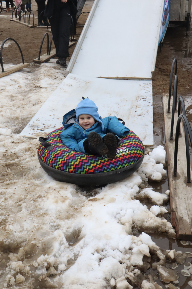 Young child in a bright blue snowsuit coming down the Ski Snow Valley mobile hill in a brightly coloured tube