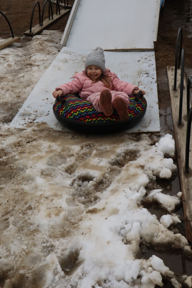 young child in a bright pink snowsuit coming down the Ski Snow Valley mobile hill in a brightly coloured tube