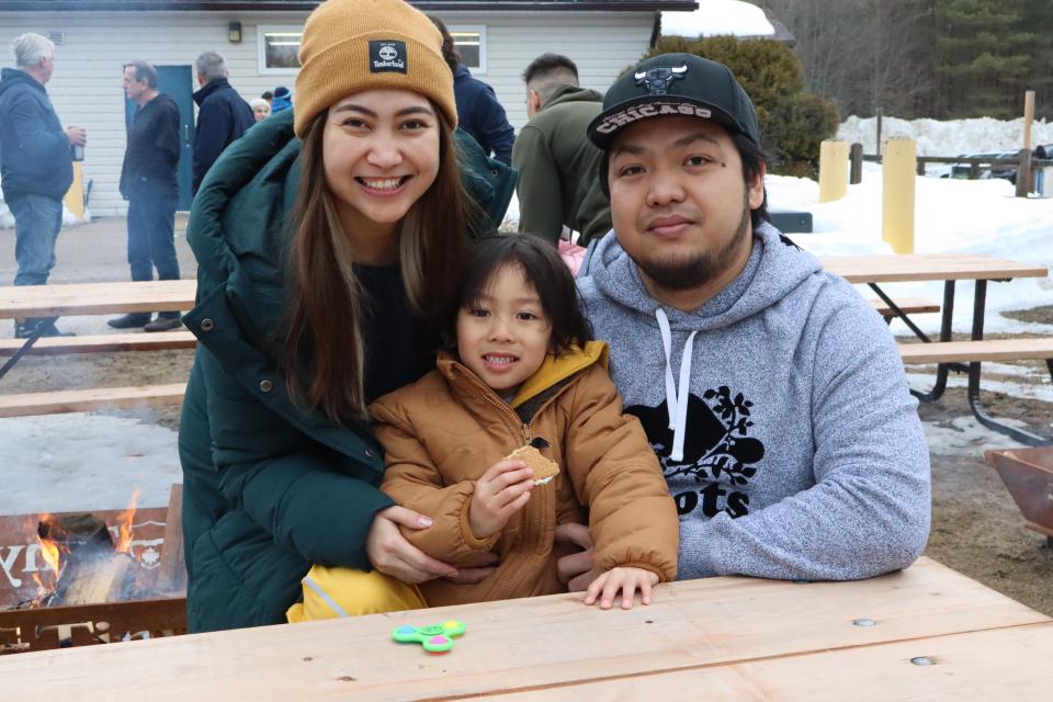 Young family sitting at the picnic tables near the fire pits as the child enjoys a s'more treat