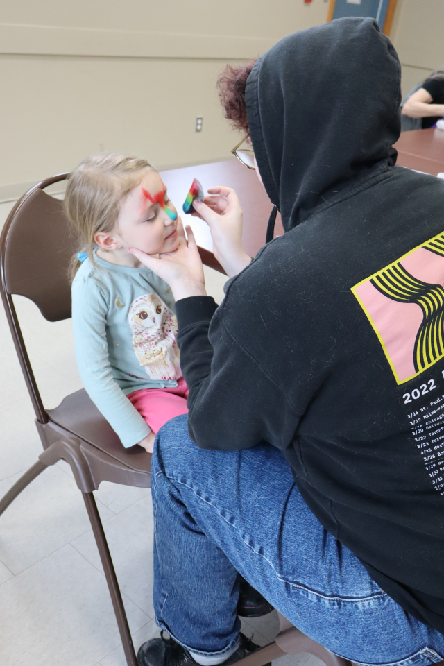 Face paint artist painting a rainbow design on a young girl's face