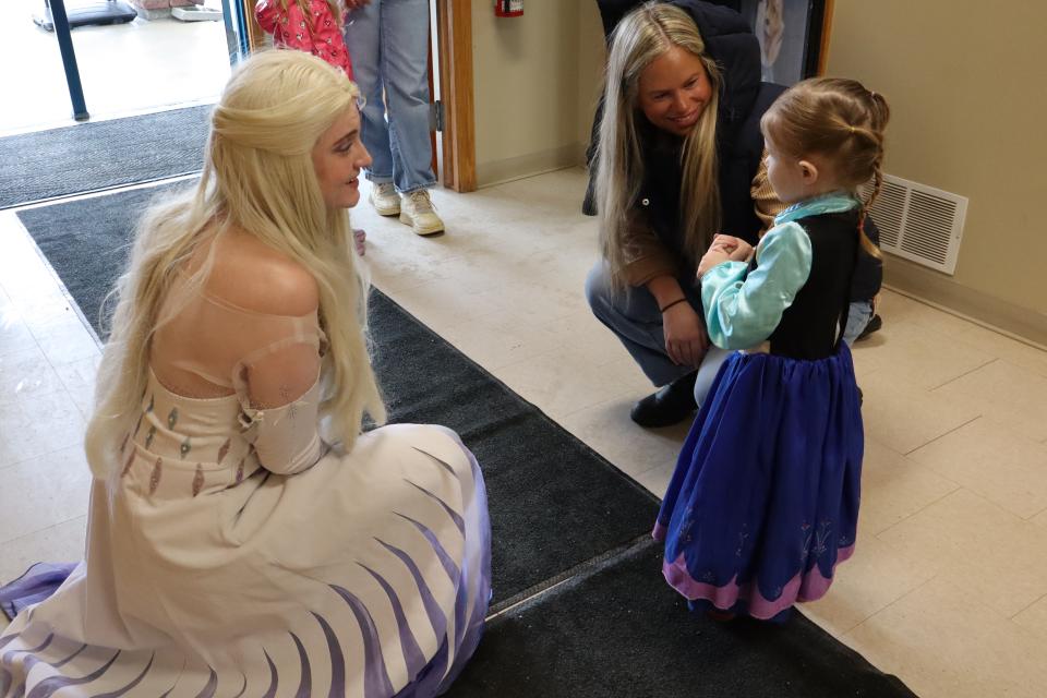 Elsa from Frozen singing to a young girl dressed as Ana from Frozen with mom looking on with smiles