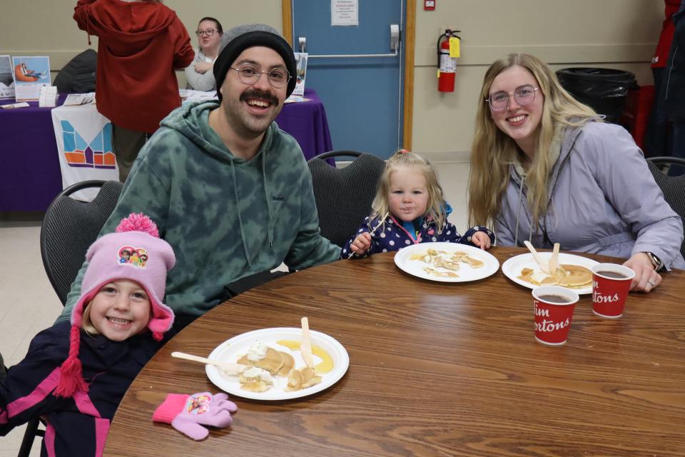Young family with two small children sitting at a round table enjoying their pancake lunch