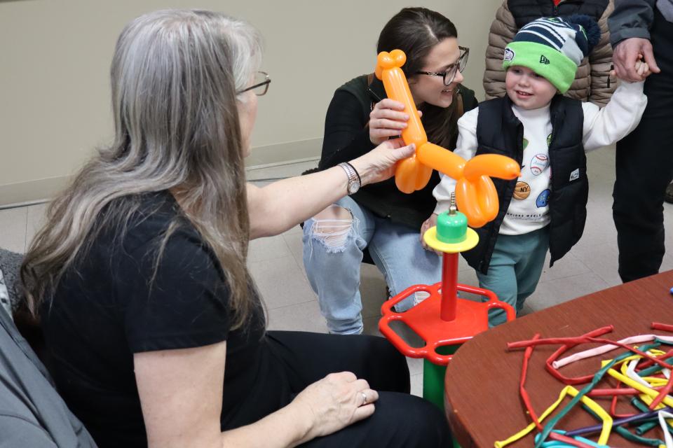 Young child with an excited mom receiving a balloon animal from the balloon twister