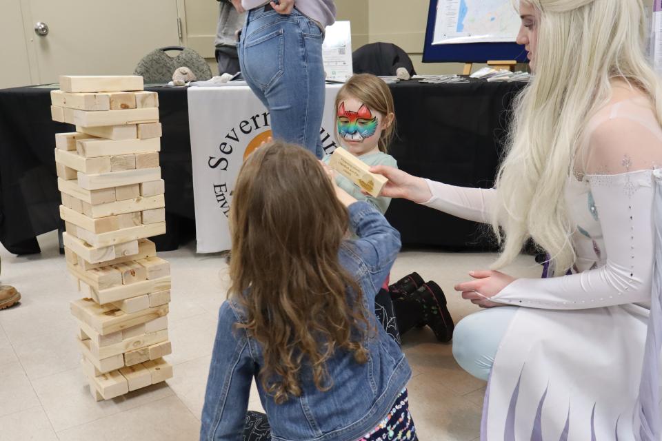 Elsa and two girls, one with bright rainbow facepaint building the Severn Sound Environmental Association's branded block tower