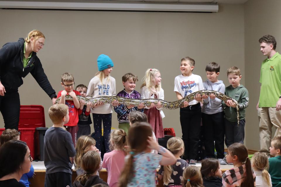 Group of several children standing in a row holding a large snake