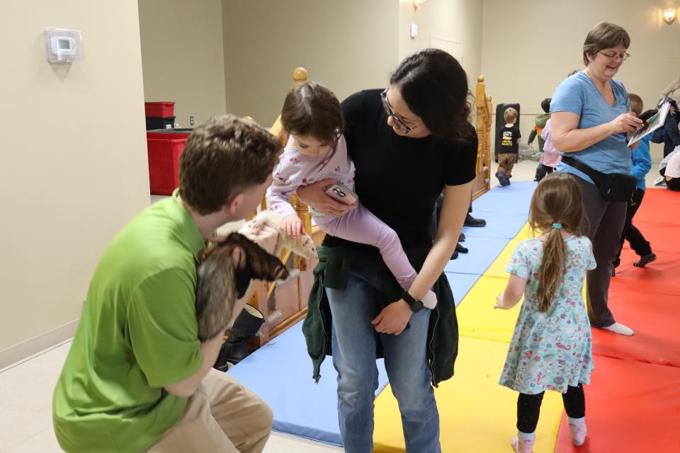 Mom carrying young child visiting with the ferrets