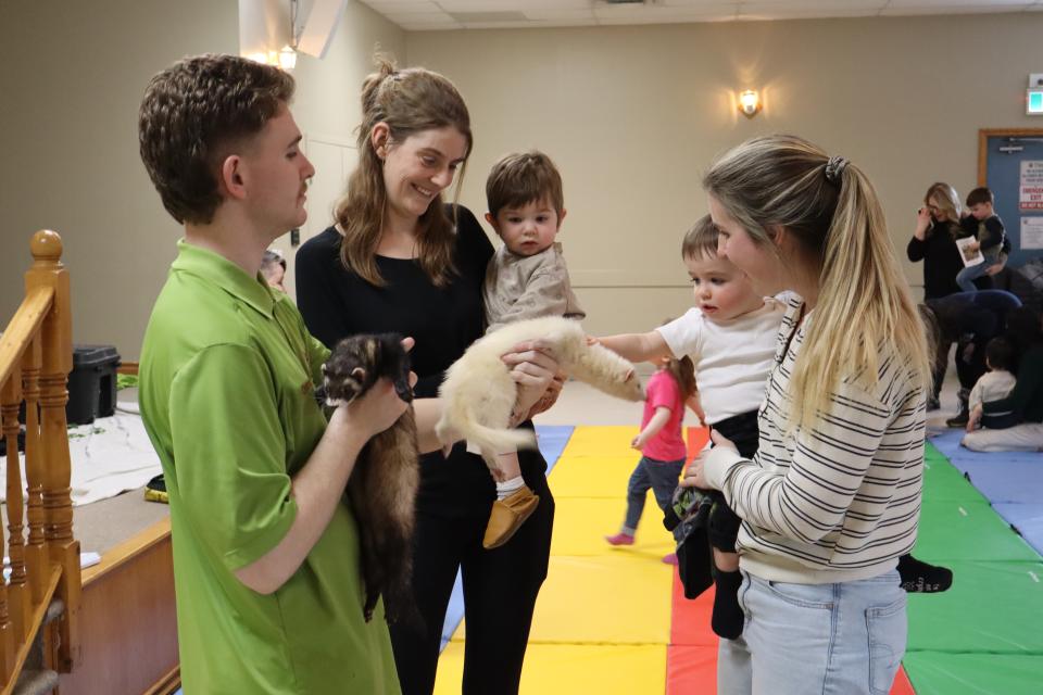 Two moms carrying their young children come to pet the ferrets the Zoo to You staff is holding