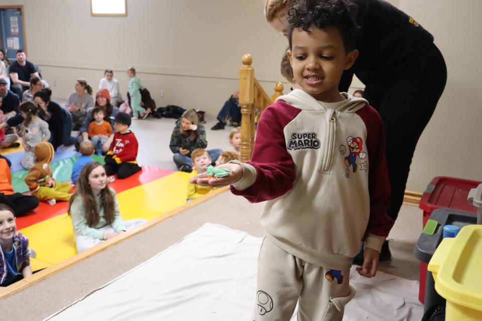 Young boy standing on stage with a bright green frog in their hand