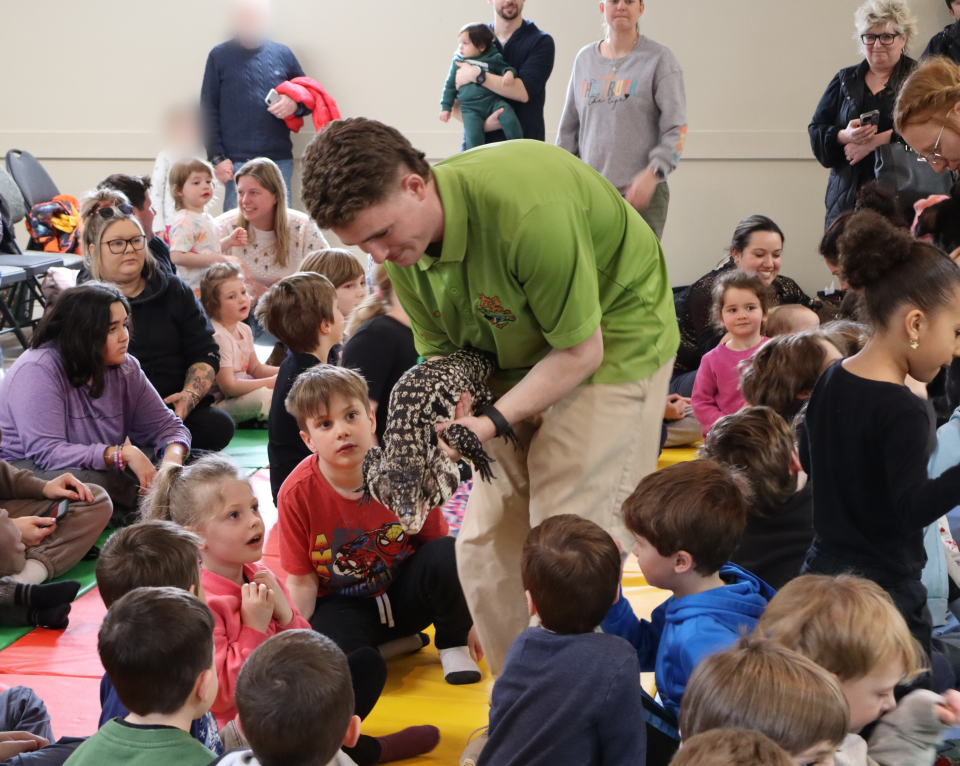 Zoo to You staff bringing a large lizard through the crowd of children