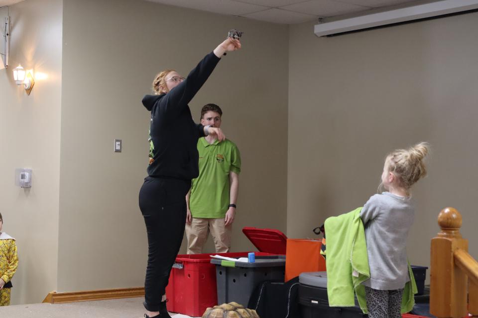 Zoo to You staff holding the sugar glider high in the air with a young girl equipped with a towel and cloth bag for the animal to land on