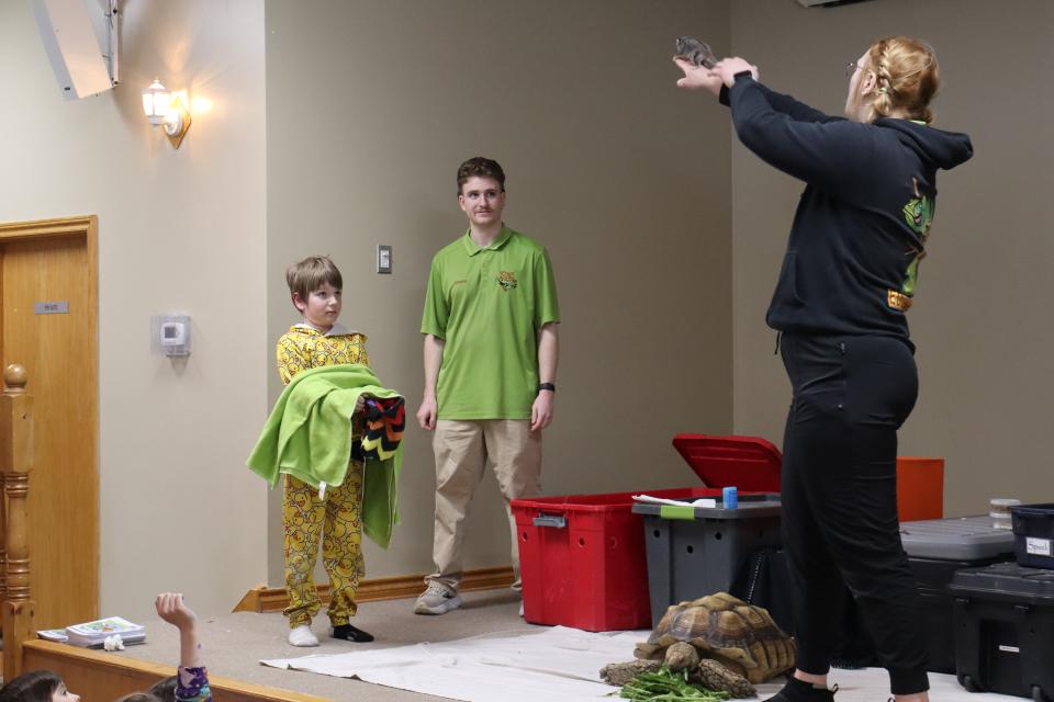 Zoo to You staff holding a sugar glider high up in the air so it can jump onto the towel and cloth bag a young boy is holding