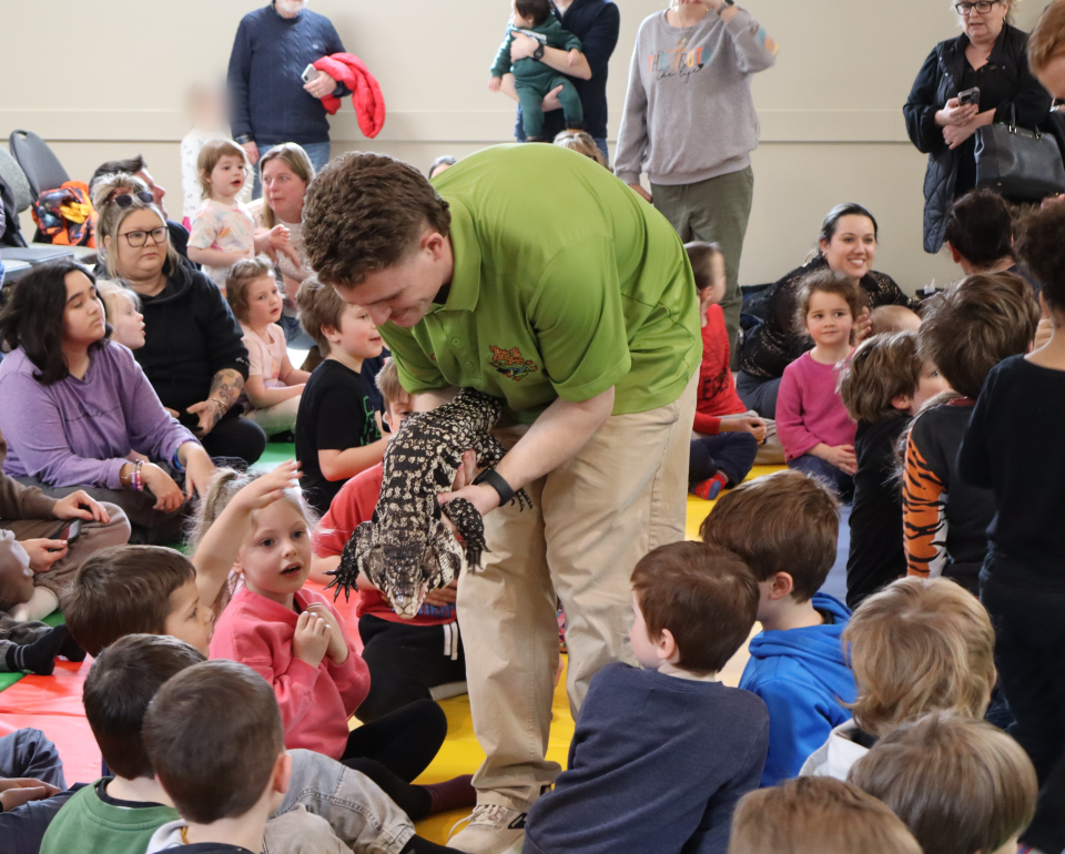 Zoo to You staff bringing the large lizard around the crowd of children, with the kids looking on in excitement