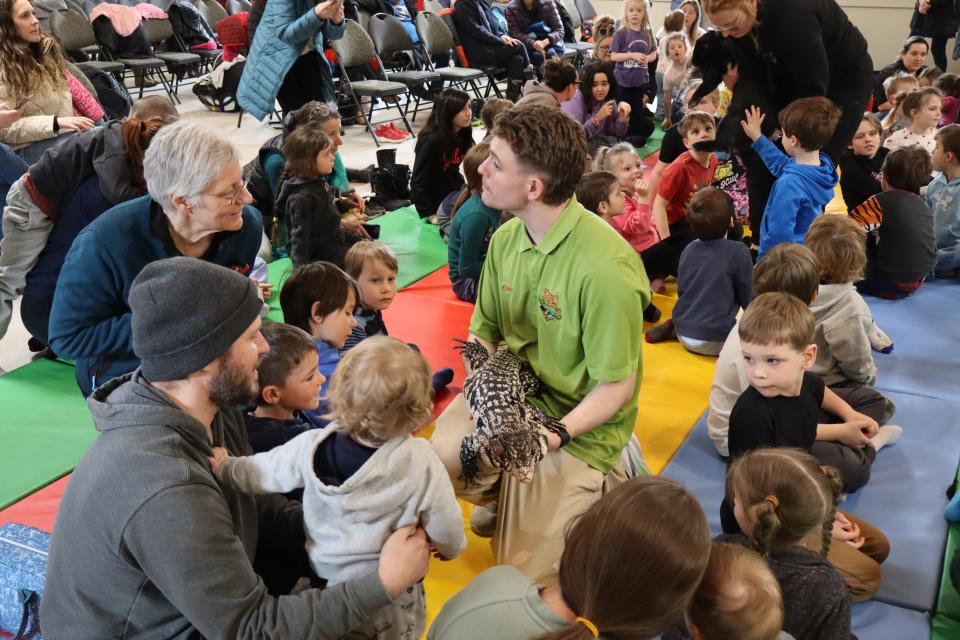 Zoo to You staff sitting amongst the crowd holding a large lizard