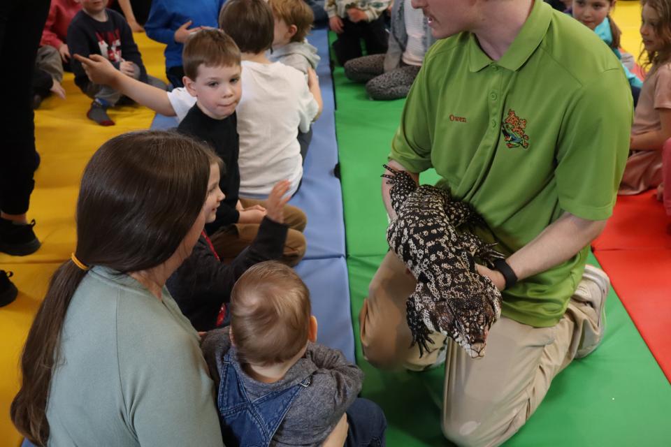Zoo to You staff holding a large lizard with mom and young children looking on