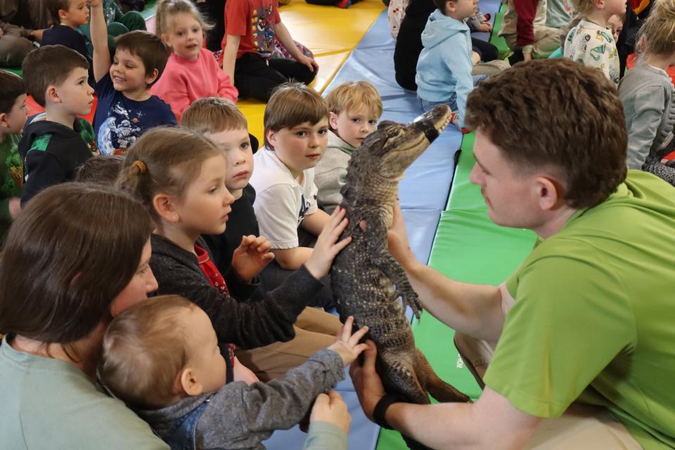 Zoo to You staff holding a crocodile while children reach out to pet their back