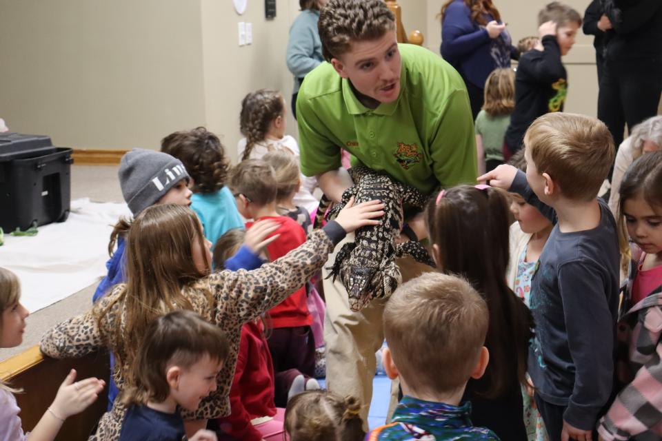 Zoo to You staff holding the large lizard as children reach to pet the back of it