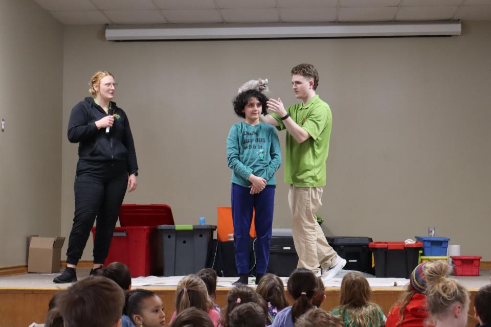 A chinchilla is being placed on a boy's head on stage by Zoo to You staff