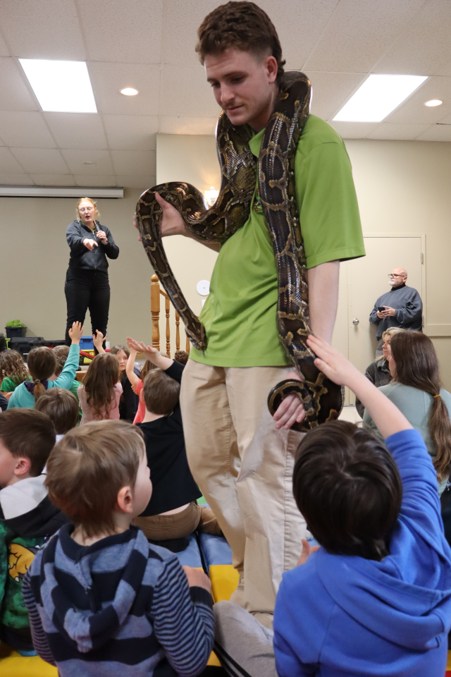 Zoo to You staff with a snake draped around their neck allowing kids to pet the snake