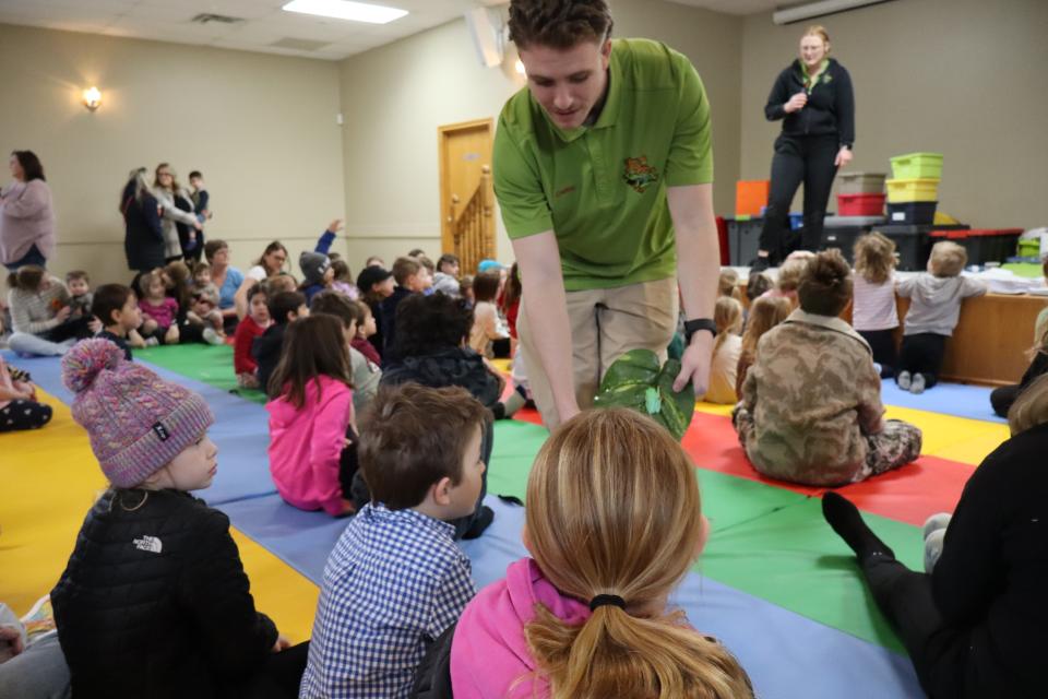 Zoo to You staff showing children the bright green frog on a large leaf