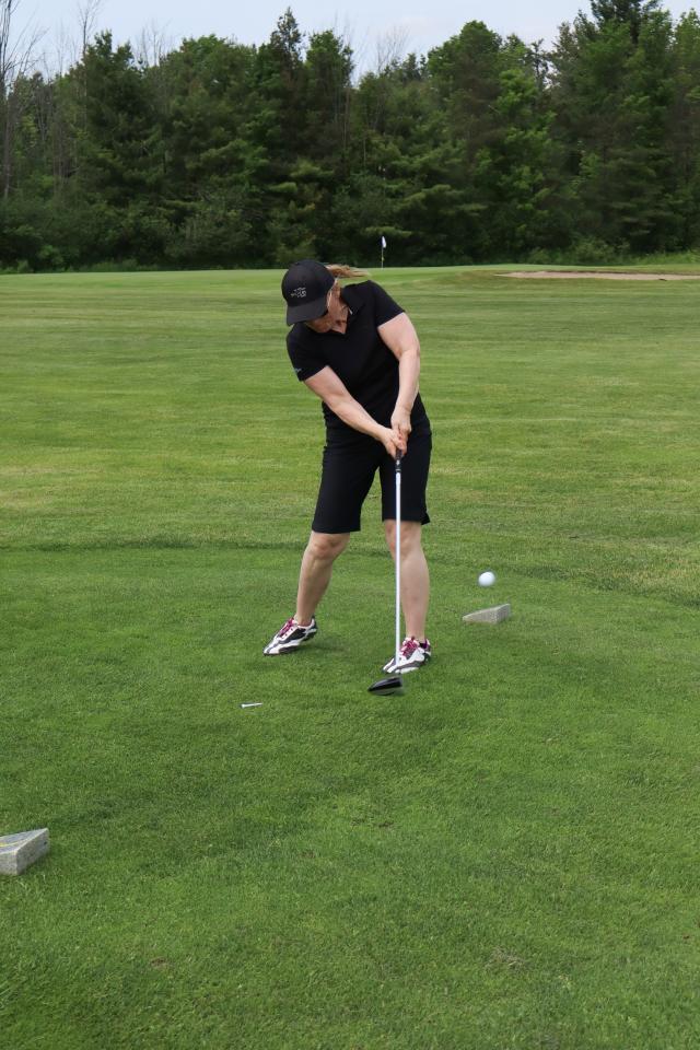 A woman as their golf swing is all the way through and the ball begins to ascend off the ground