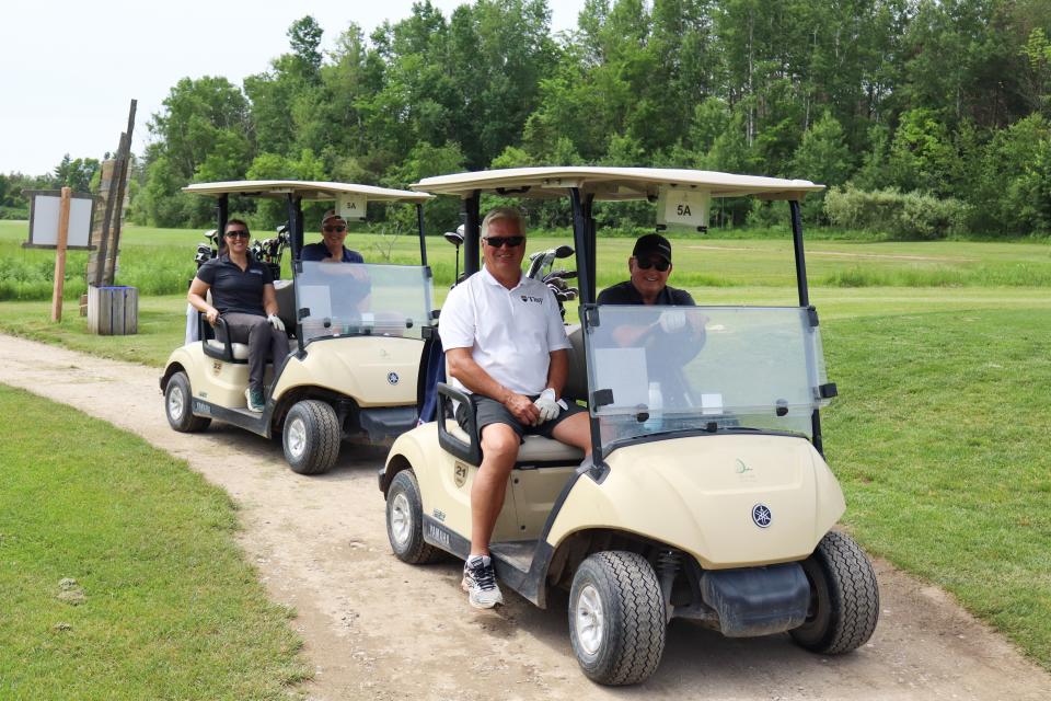 A golf foursome, including Mayor David Evans, sitting in two golf carts on a path next to the course