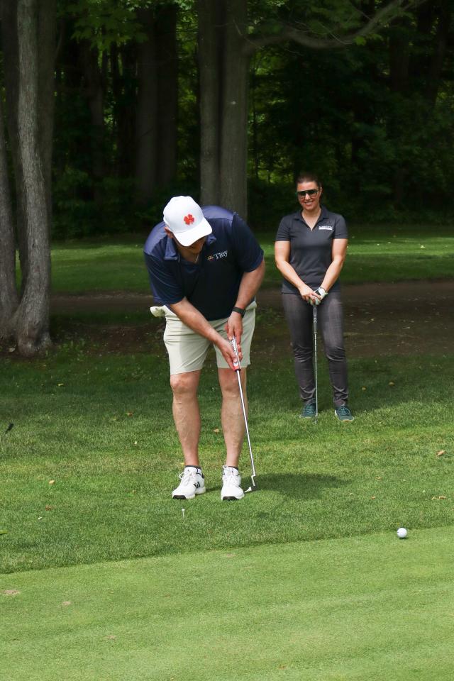 A man putting a golf ball, with a woman standing behind them