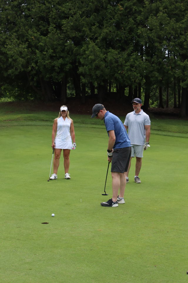 Three golfers standing on the golf green and one person is putting
