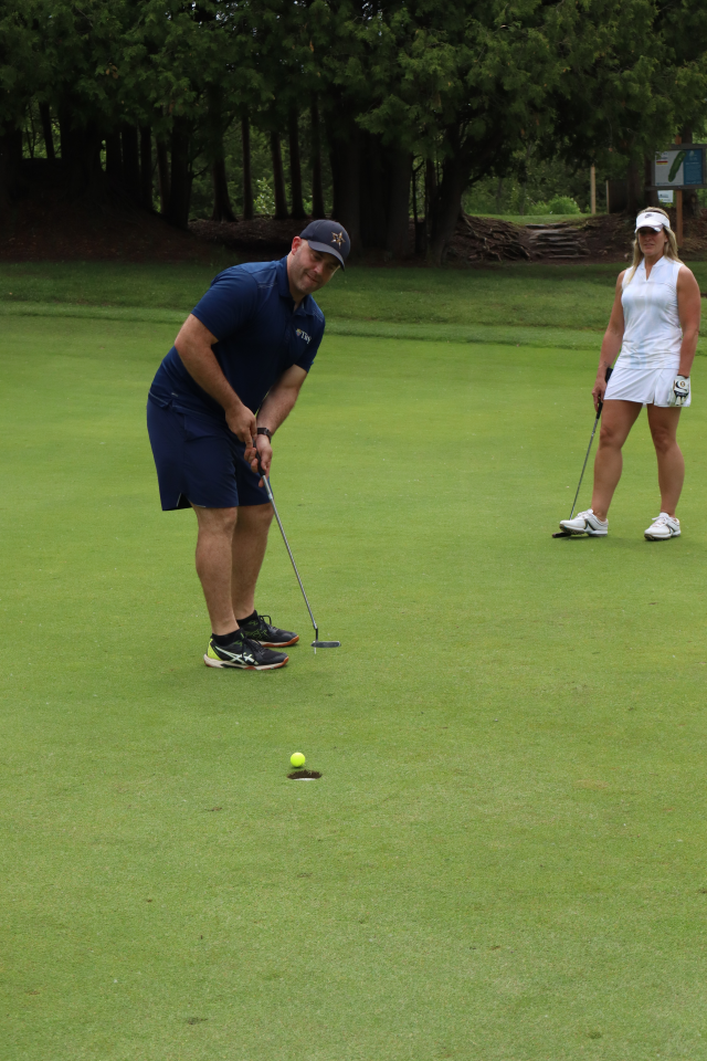 A man putting with the golf ball about to land in the hole, with a woman standing behind them
