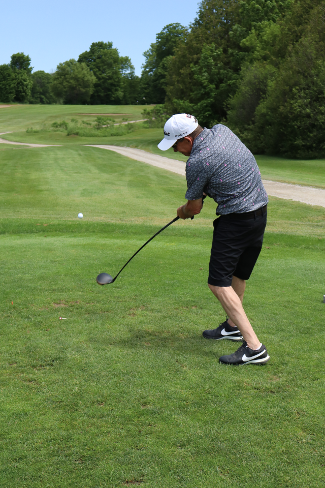 A man as their golf swing is all the way through and the ball begins to ascend off the ground