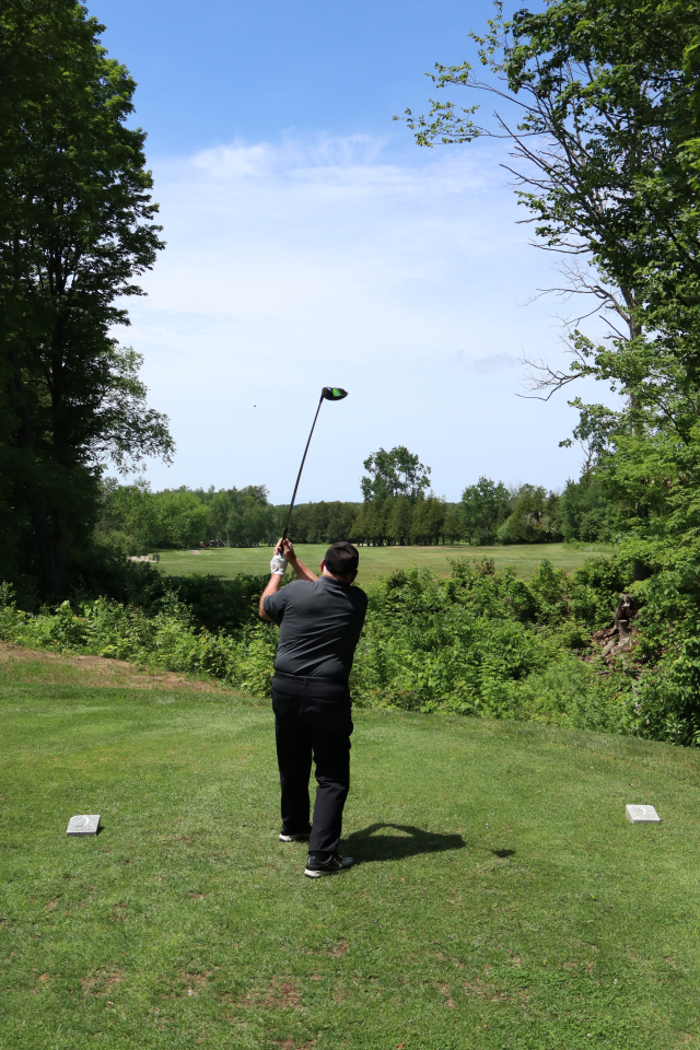 A man as their golf swing is all the way through and the golf ball is high in the sky