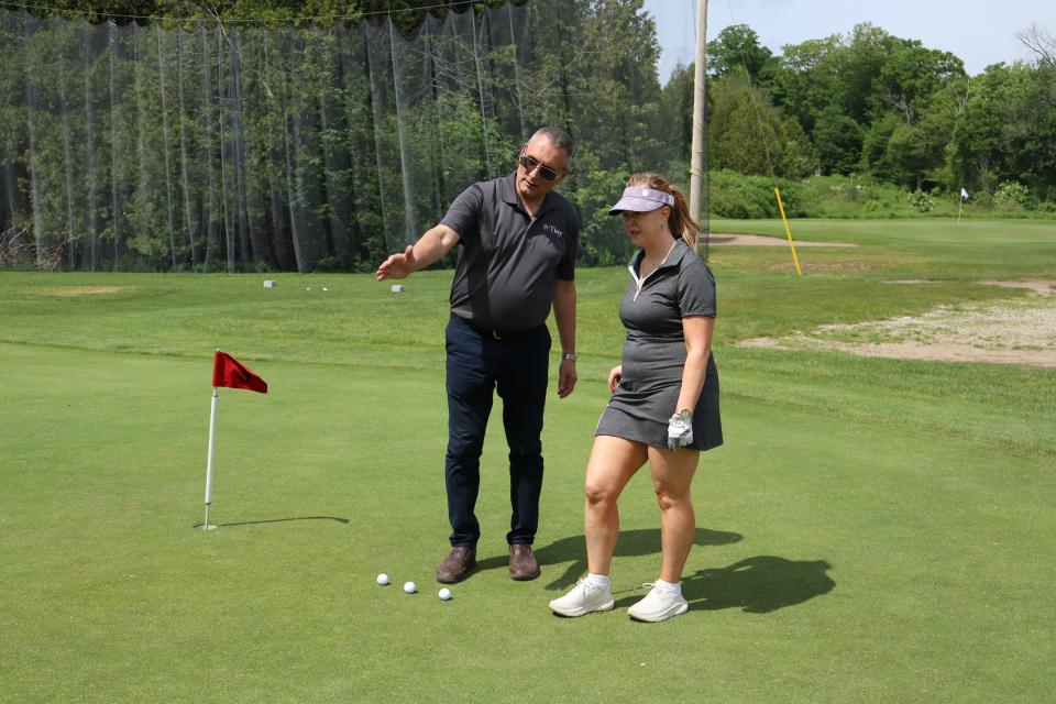 Councillor Dave Brunelle standing beside and talking to a woman on the putting green