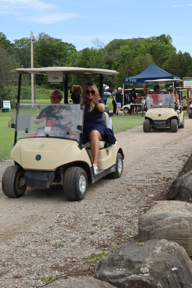 Two golf carts driving by on the path with golfers smiling and waving