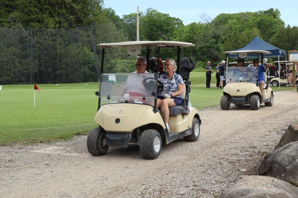 Two golf carts driving by on the path with golfers smiling and waving