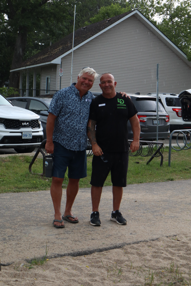 Mayor David Evans and a man in black clothing posing on the pathway with cars parked in the background.