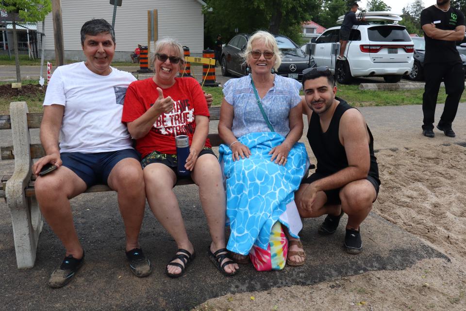 Group of four people, three sitting on a public bench on the beach.