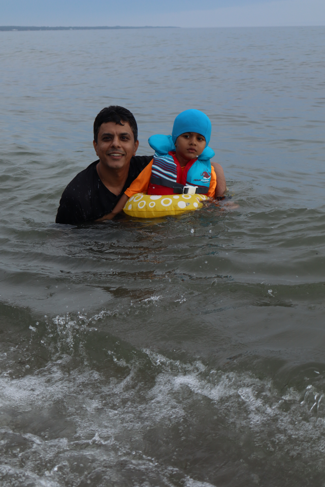 Father and son in the water, the child wearing a colourful swimsuit, life jacket, and inner tube.