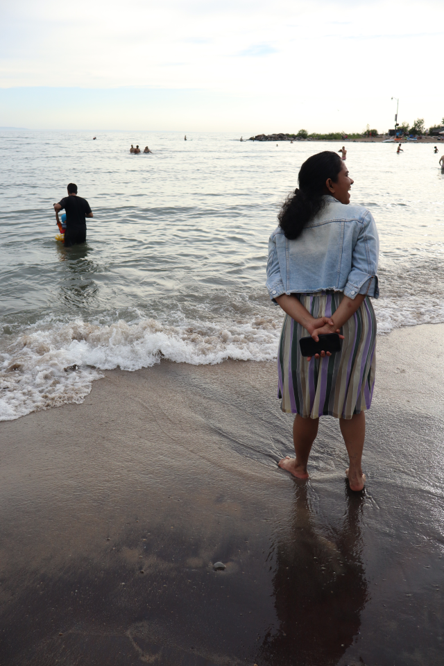 Mother standing on the beach, smiling, as the father and son go out into the water.