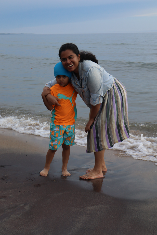 Mom and son posing at the water's edge on Balm Beach, the child wearing a brightly coloured swimsuit.