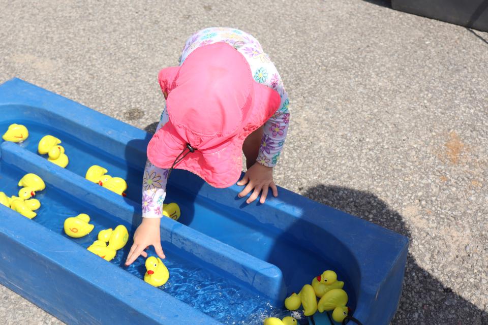 View from above a child wearing a bright pink hat reaching for a toy rubber duck.