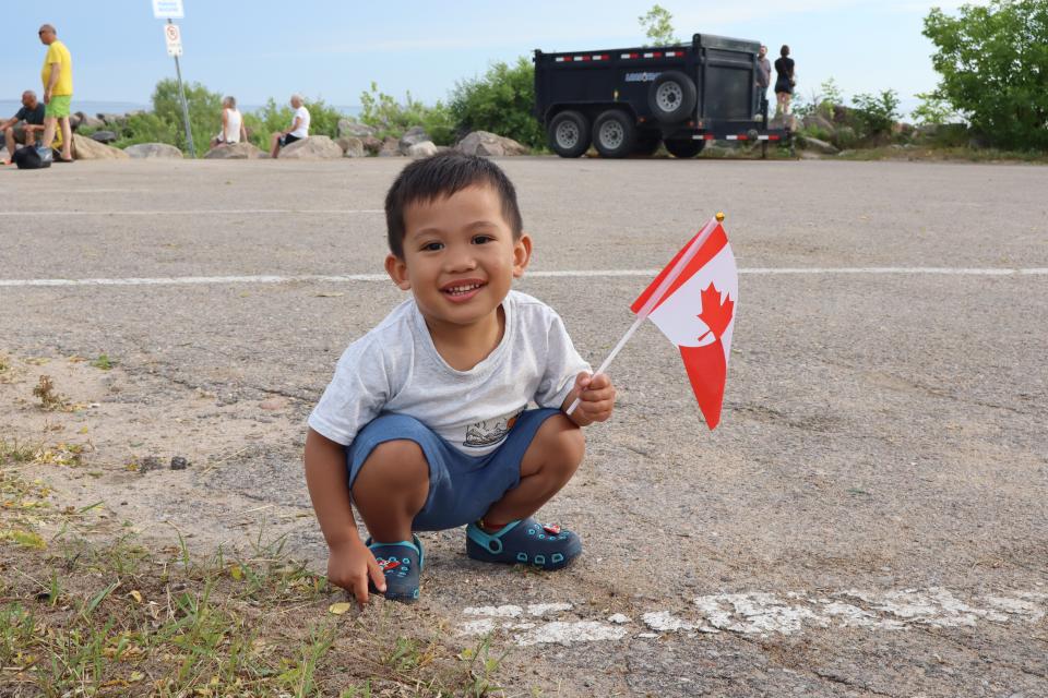 Young boy squatting down holding a Canadian flag and smiling.