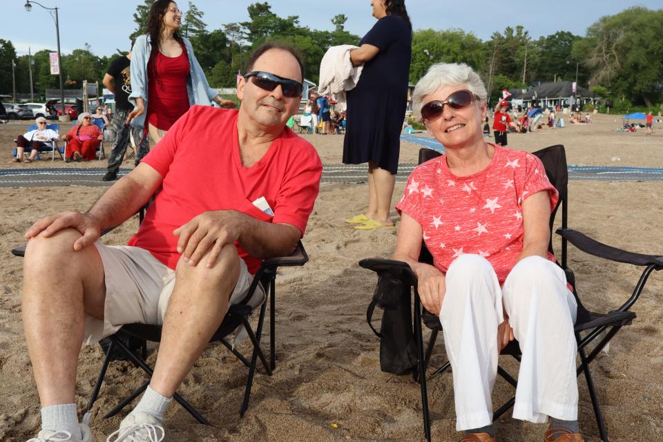 Two adults sitting in lawn chairs in the sand watching the live entertainment, dressed in red and white.