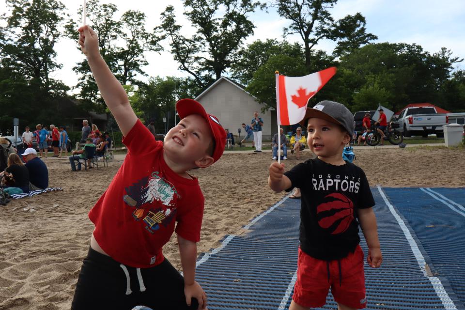 Child brothers waving Canadian flags while standing on the mobi-mat for accessibility on the beach.
