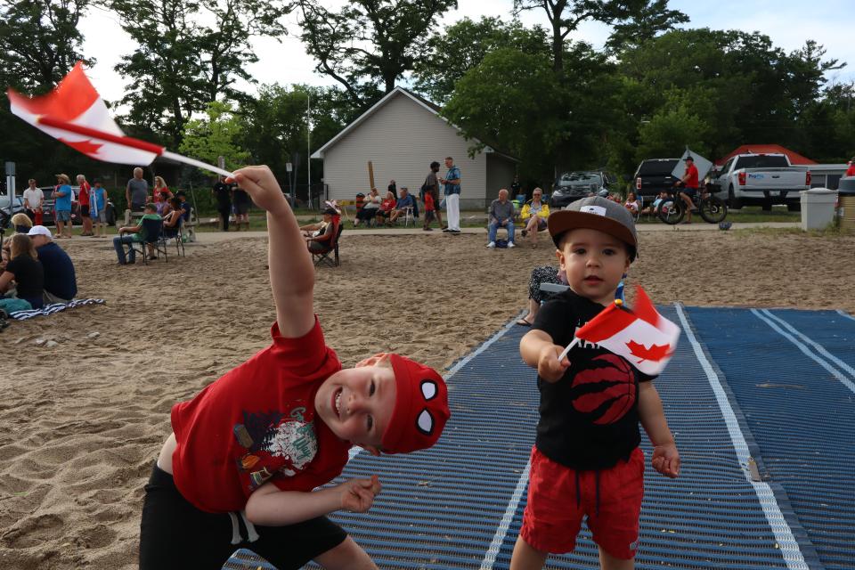 Two brothers vigorously waiving Canadian flags, one child is bent over sideways in excitement.