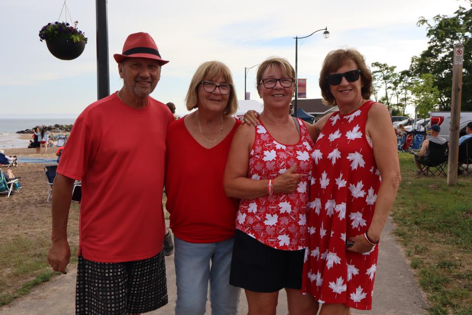 Group of four adults dressed in red and white posing together on the paved pathway with the beach in view behind them.