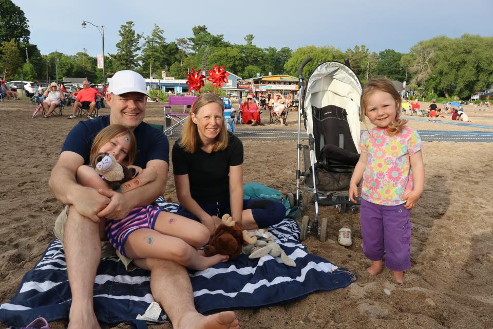 Young family with two girls enjoying the entertainment from a beach blanket set up in the sand.