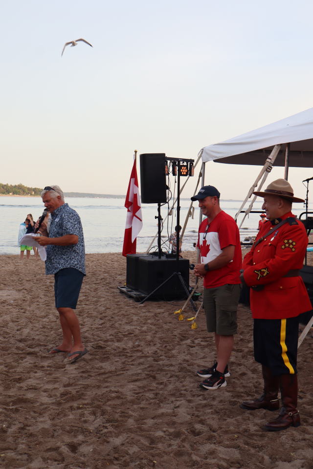 Mayor David Evans giving a Canada Day speech with Deputy Mayor Sean Miskimins and Councillor Kelly Helowka standing in front of the stage.