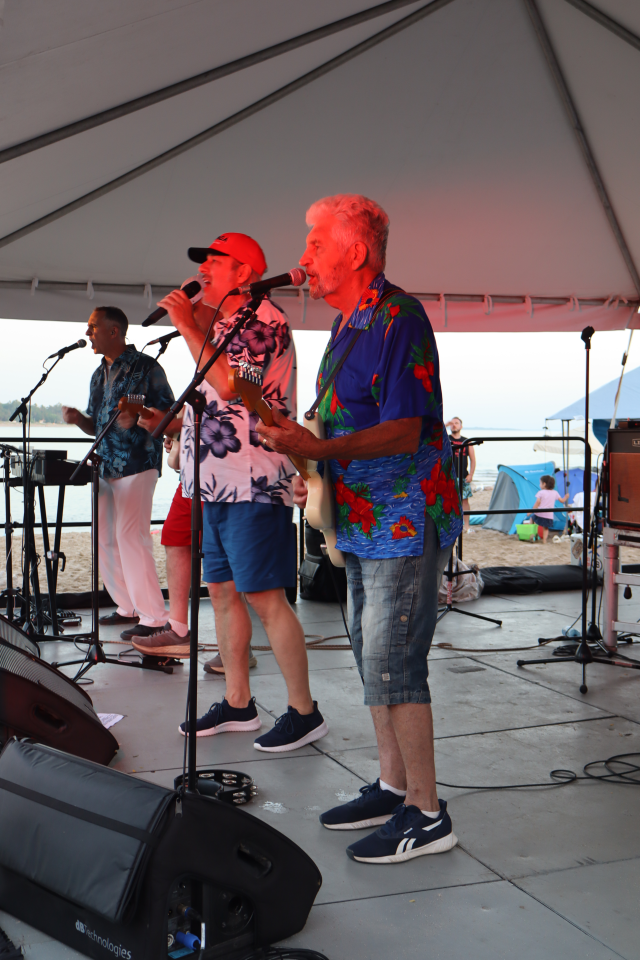 Three members of the Beach Bums band performing live on stage.