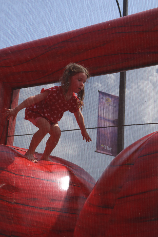 Child getting ready to jump from one large red ball to another in a bouncy castle with a mesh layer of protection.
