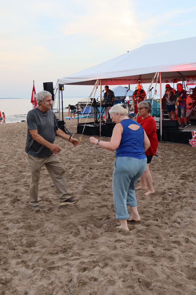 Man and two women dancing in the sand in front of the stage.