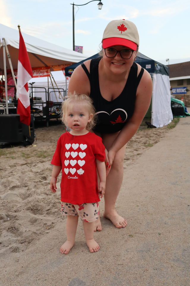Mom and daughter wearing Canada Day clothing standing on a pathway near the sand.